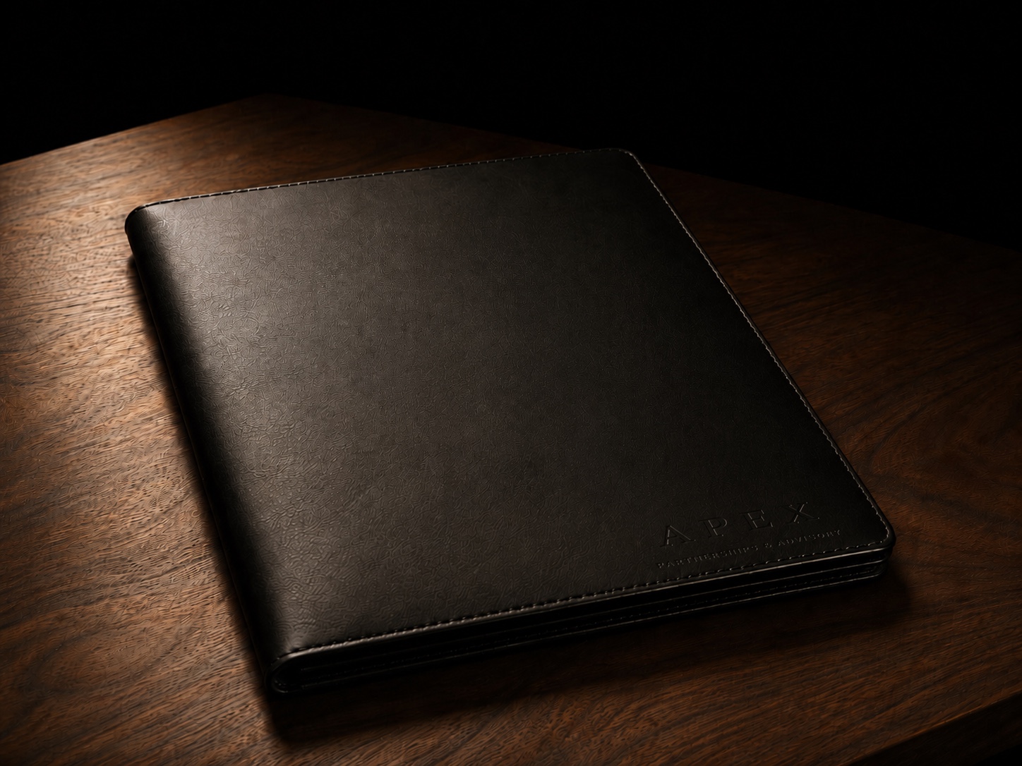 Een zwarte leren folio met het Apex-woordmerk erin geëmbosseerd, op een walnoten bureau